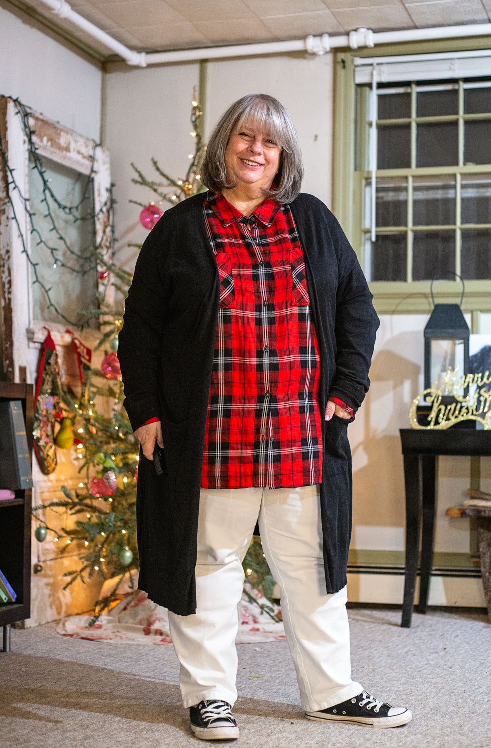 bettye wearing red plaid buttondown and black cardigan in front of christmas tree