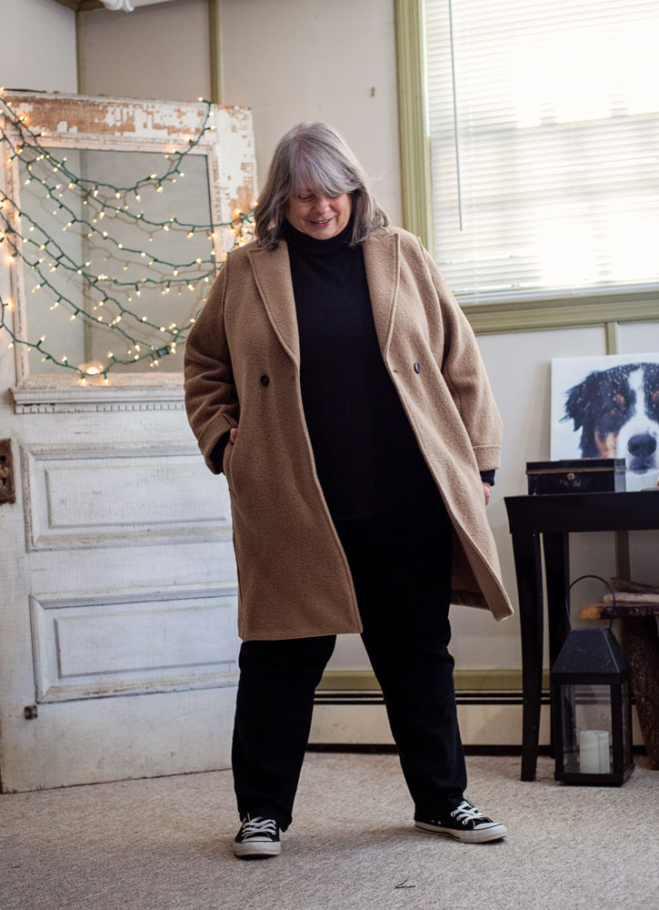bettye standing in living room in a camel coat