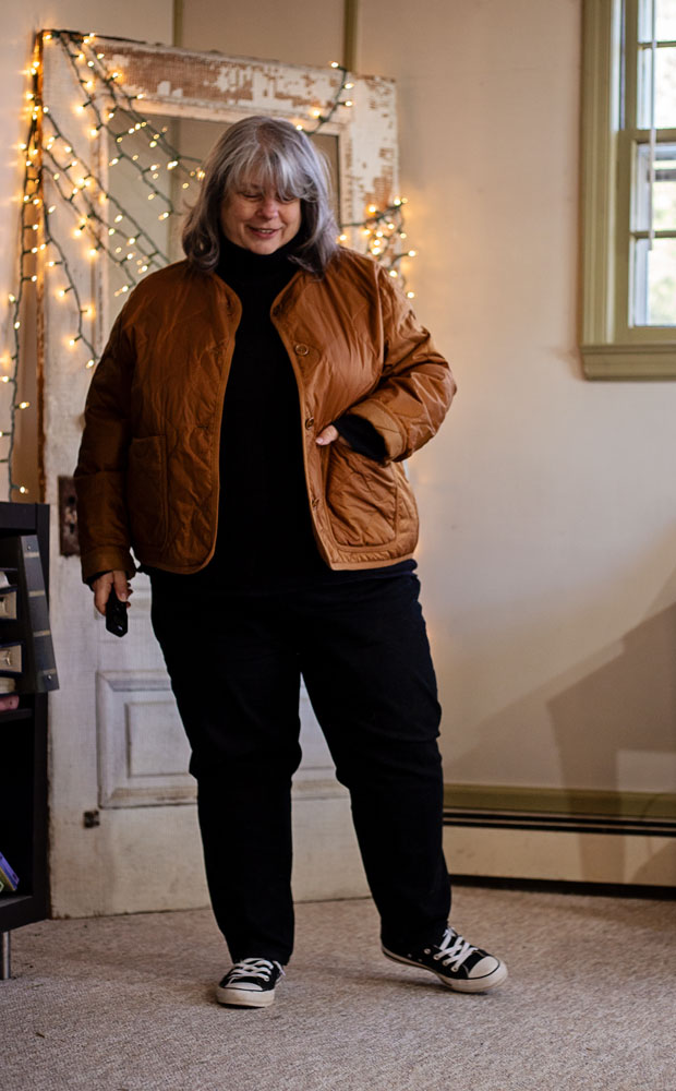 bettye standing in front of twinkle lights in black outfit and brown jacket