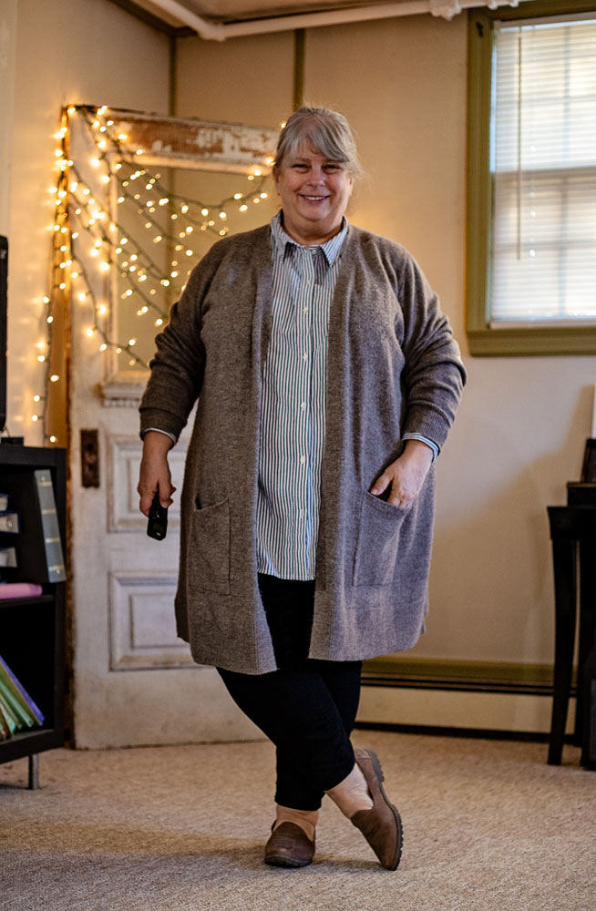 bettye standing in living room in taupe cardigan and striped buttondown