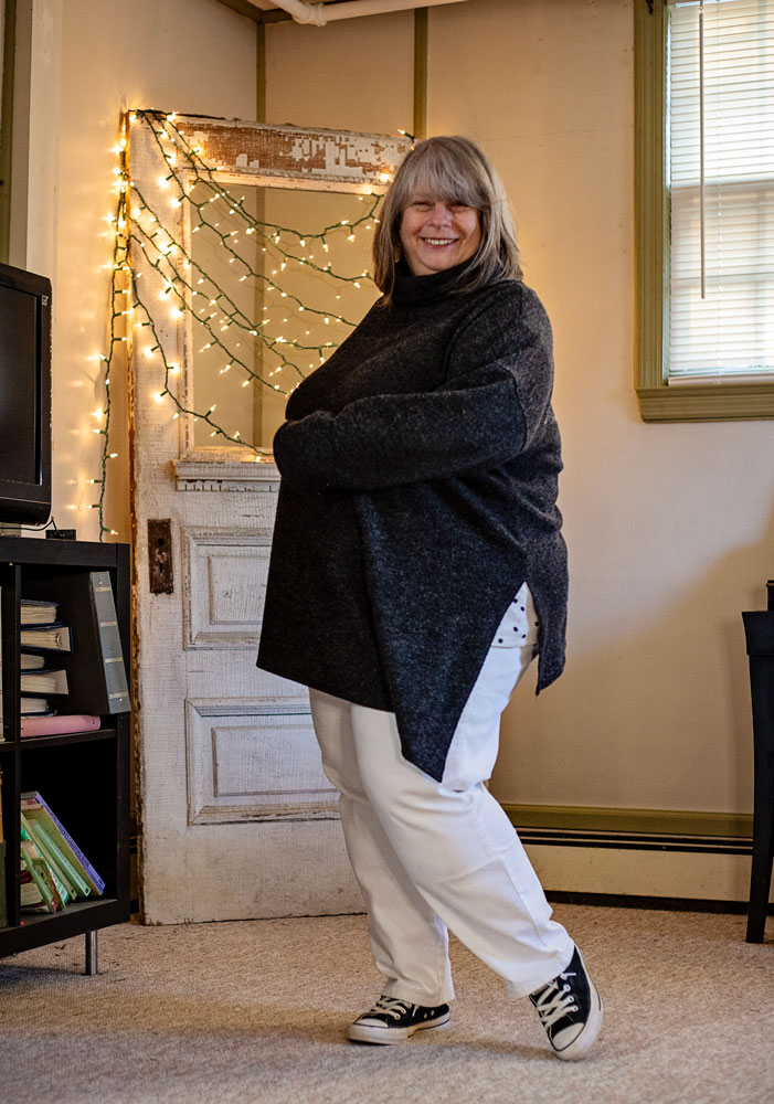 bettye standing in living room in dark grey sweater and white jeans