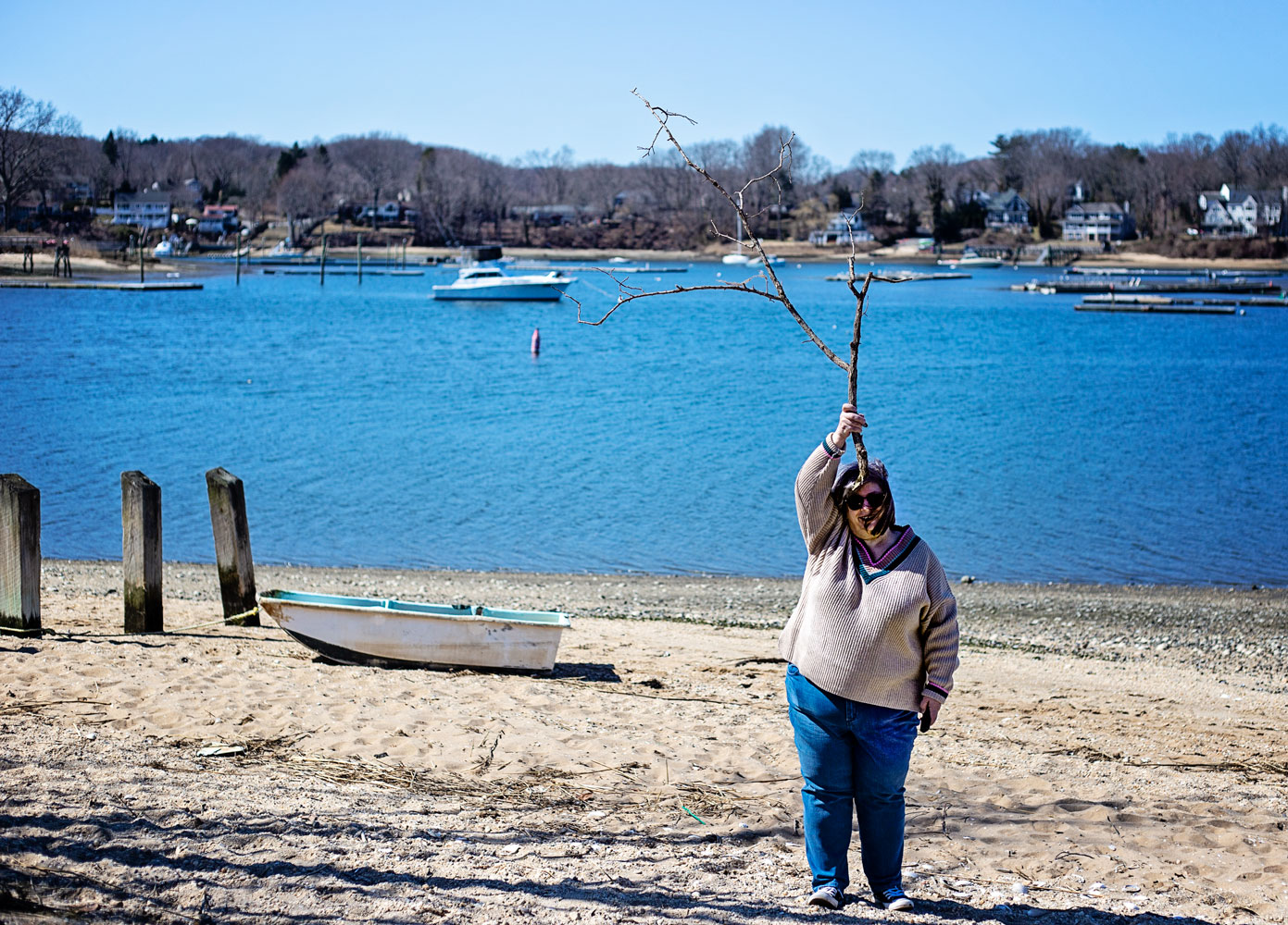 bettye standing on the beach by the harbor with a big tree branch on her head