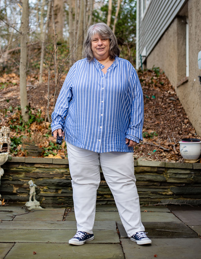 bettye standing outside on patio in white jeans and bloue striped buttondown shirt