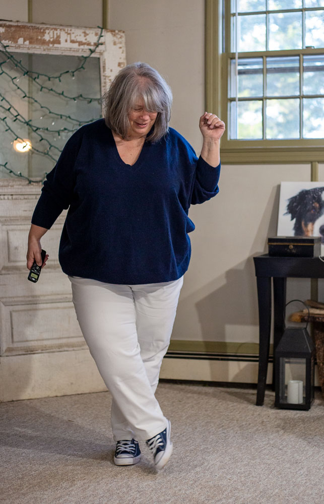 bettye standing in front of an antique door with twinkle lights wearing a navy v-neck sweater and white jeans