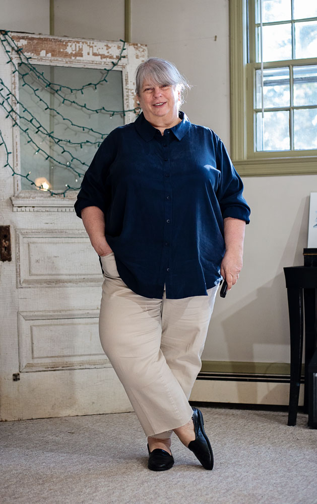 bettye standing in living room in khaki cropped jeans, black flats, and a navy button-down blouse